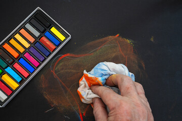 Artist's hand cleaning a black surface with a cloth, smudging colorful chalk pastels © Floren Horcajo