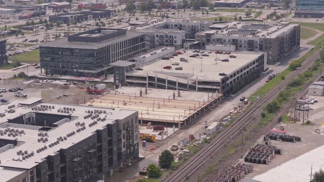 Drone aerial of new building construction of parking garage structure being structured and built by contractor crew at modern apartment complex for rental property tenants to park cars and vehicles 4k