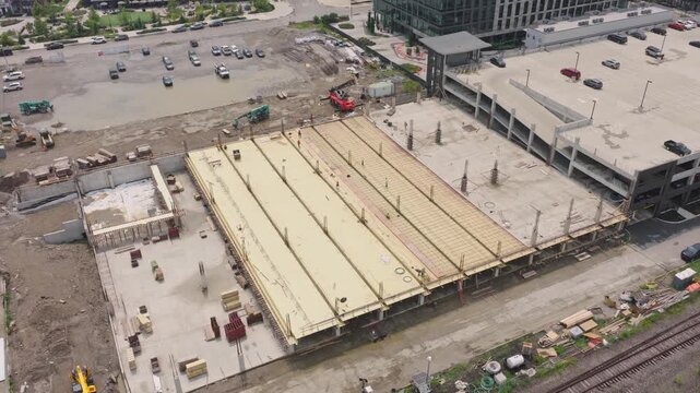 Drone aerial of new building construction of parking garage structure being structured and built by contractor crew at modern apartment complex for rental property tenants to park cars and vehicles 4k