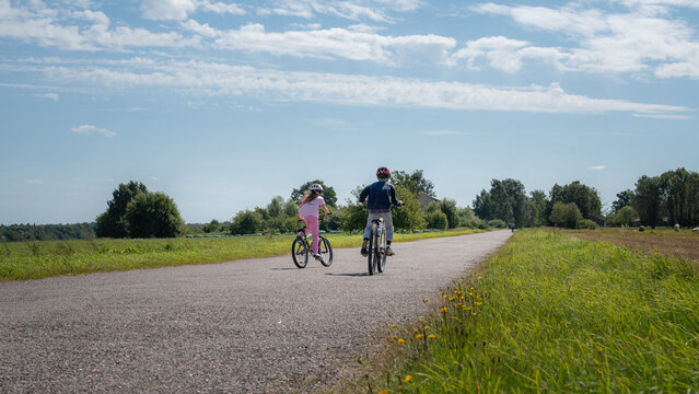 Two children riding bicycles together on a quiet rural road in summer countryside