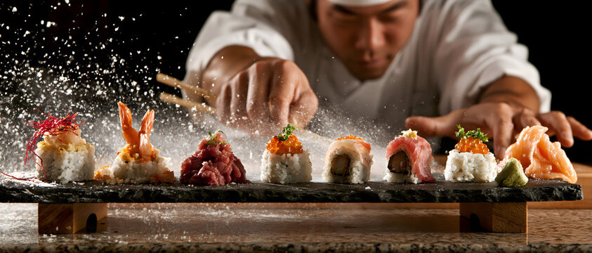 Assorted sushi rolls with chef sprinkling garnish on a slate serving platter maki nigiri sashimi raw fish seafood rice seaweed nori wasabi ginger