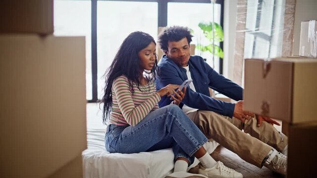 Diverse spouses moving apartment planing future interior. Couple sitting floor