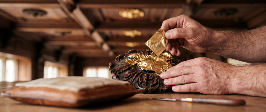 Artisan gilding wooden ornament with gold leaf hands restoring antique decorative carving
