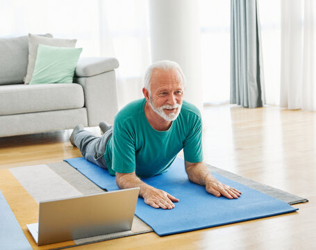 Senior man exercise stretching yoga using laptop online instructions at home health care