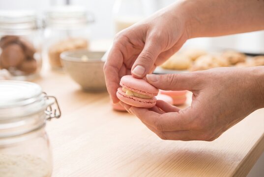 Close up of female hands gently pressing two pink macaron shells together with cream filling