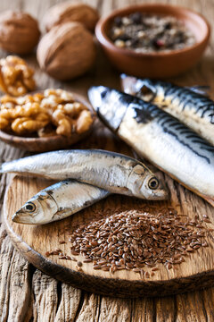 Close-up of sardines, mackerel, flax seeds, and walnuts on a wooden surface under natural lighting with various spices