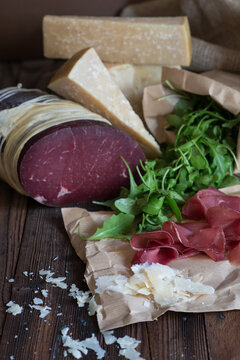 Close-up of a whole muscle of bresaola, blocks of parmesan cheese, cheese shavings  and rocket on a  wooden table