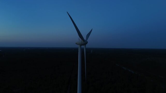 drone footage of wind turbines standing in a row above a forested landscape during the evening showing renewable energy infrastructure and industrial development in northern nature