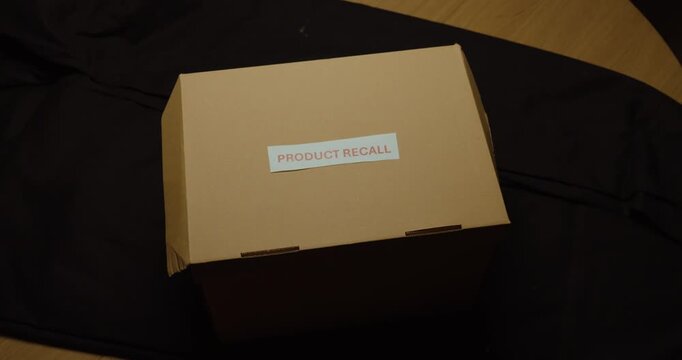 Person placing a Product Recall label on a package. Ideal for defective products, quality control, product safety, returns and recall procedures.