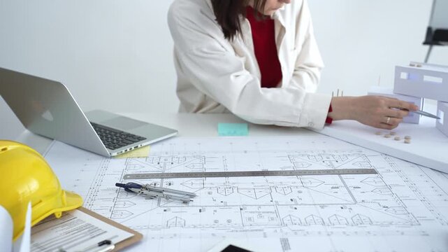 Architect working on new residential project using laptop, reviewing blueprints and drafting floor plans for modern building design with a 3d model on office desk