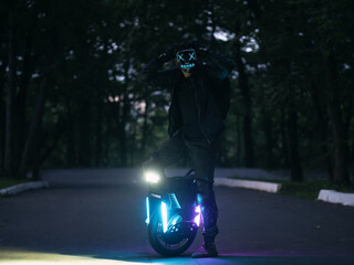 A man poses in a park on an electric monowheel wearing a luminous mask. Halloween Time © pavelkant