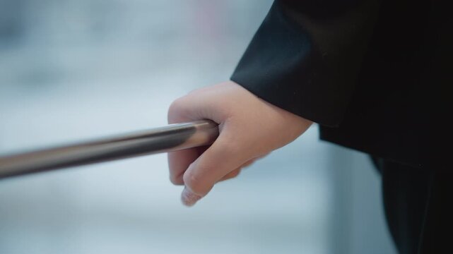 Right hand wraps firmly around metal handrail with slight forward pull, suggesting steadying movement during descent; dark long sleeve adds formal look inside modern building with calm atmosphere