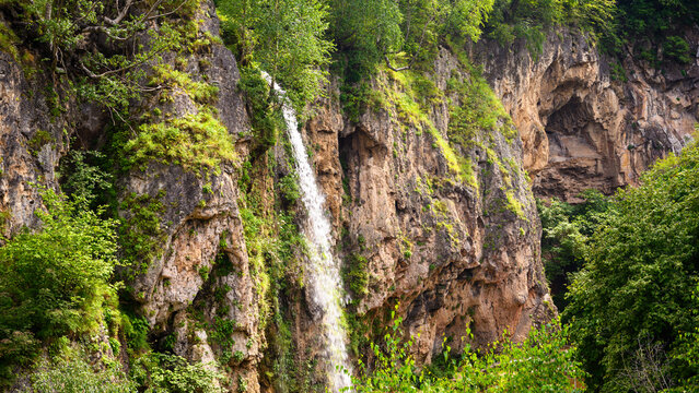 Waterfall cascading down a steep rock in canyon in summer. Natural landscape with green vegetation and rugged stone face. Outdoor wilderness scenery