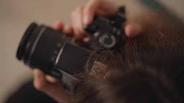 Hands work camera controls in close view, fingers turning lens ring and mode dial while grip stays steady, creating focused setup, precise handling, and clear preparation indoors, with camera, hand