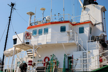  White ship superstructure with red trim and life buoys against a clear blue sky, showing the bridge deck of a docked vessel © Татьяна Швец