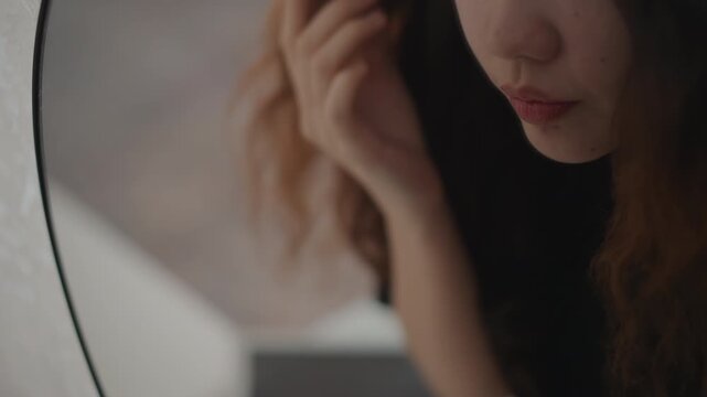 Close-up view shows young woman carefully applying eye makeup while looking into mirror, with subtle hand movement, gentle head tilt, and calm focused beauty routine indoors, with woman, makeup