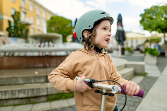 Young boy wearing a safety helmet rides a kick scooter on a city sidewalk. Active childhood, urban mobility and road safety for children.