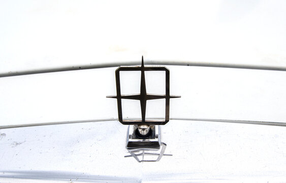 Close up of classic Lincoln hood ornament mounted on white vehicle. Iconic four pointed star emblem stands upright on chrome trim piece, casting slight reflection