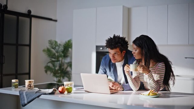 Family couple looking computer at kitchen holding morning coffee cups closeup