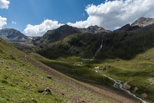 panoramic view to a valley between mountains with flowing river and waterfall on a sunny day
