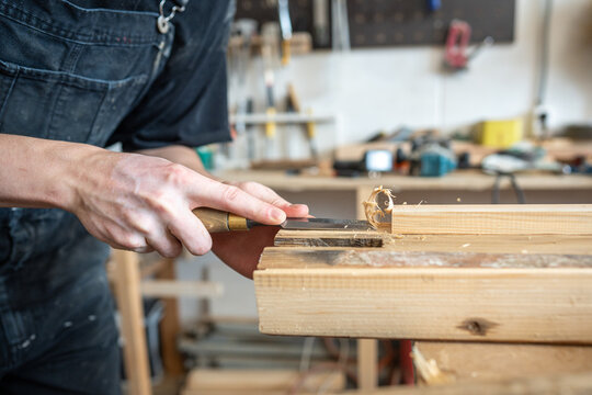 Wooden board preparation process for restoration in carpentry workshop, master chisels wood surface, professional restorer removing old layers from part of board with chisel instrument at workplace.