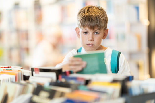 Teenage boy stands in bookstore, browsing shelves and picking out book that interests him