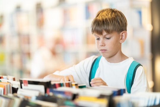 Interested teen male visitor holding a book near display stand in public library