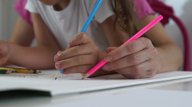 Angle shot capturing mother and child hands holding colored pencils to complete a sea life art project.