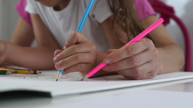 Low-angle close-up shot of mother and daughter's hands coloring simultaneously on a paper template.