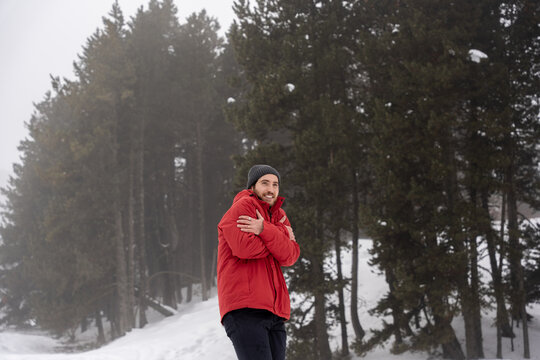 Young man shivering from cold hugging himself for warmth in foggy winter forest