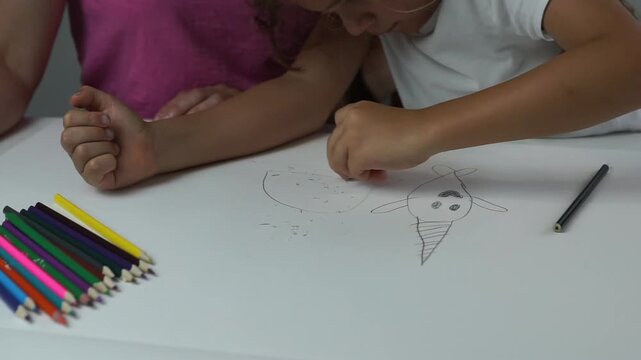 Close up of a little girl's hands using a rubber eraser to clean up pencil lines on her drawing paper at a desk.