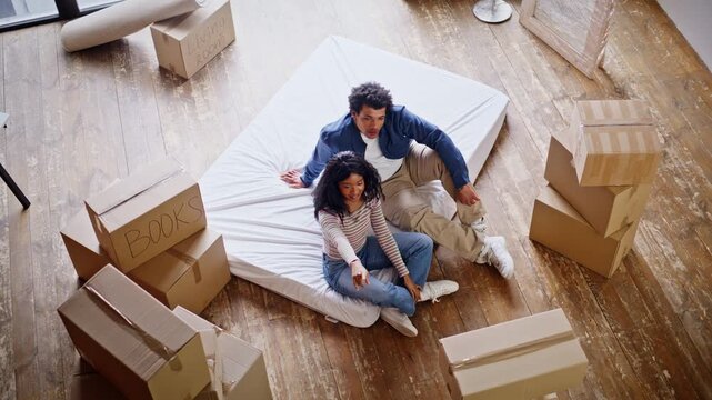 New homeowners sitting mattress around cardboard boxes discussing future design