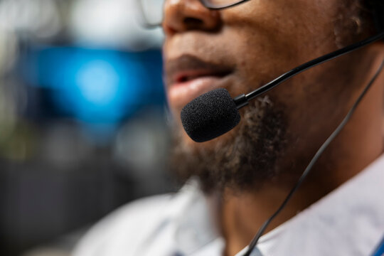 Close-up of a headset microphone shows an administrator speaking with clients during a remote support call, managing service tickets and using a computer to diagnose technical problems in the office.