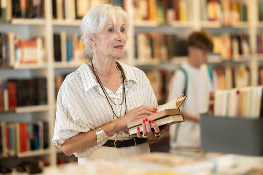 Happy senior woman choosing books from display case table in bookstore