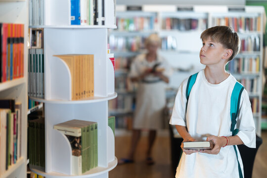 Teenage boy stands in bookstore, browsing shelves and picking out book that interests him