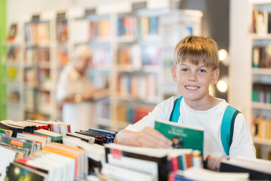 Teen boy customer flips through book in sales area of store or library, picks up reading material, hobbies or way to pass evening.