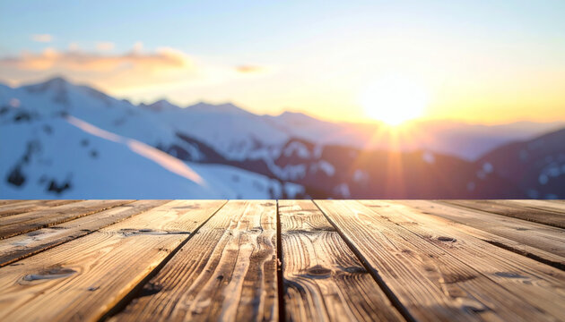 Empty wooden table surface in front of blurred snowy mountain peaks during a beautiful golden sunset in winter landscape
