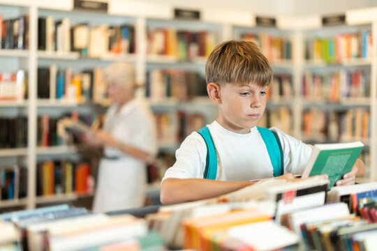 Attentive teenage boy choosing books from display case table in bookstore