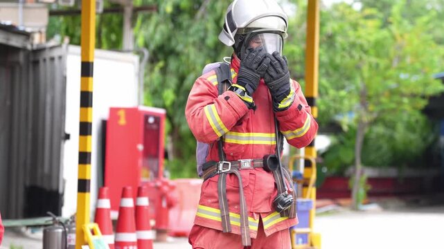 Firefighter protective suit respirator helmet glove safety emergency training first responder in red turnout gear checking equipment outdoors at fire station yard, hazmat chemical spill drill site