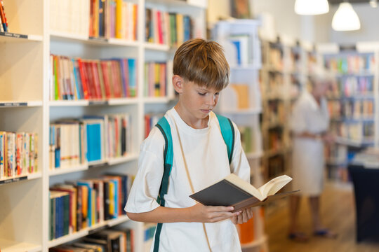 Teenage boy stands in bookstore, browsing shelves and picking out book that interests him