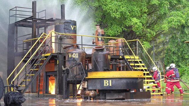 Industrial fire firefighting firefighter factory emergency smoke water spray safety responder training drill, protective crew with hose extinguish refinery mockup blaze, heavy steam rising near trees