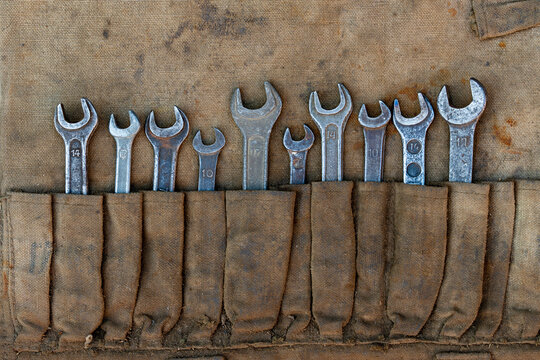 Vintage open end wrenches set in canvas tool roll organizer. Closeup old used metallic spanners in dirty fabric pouch toolkit for car repair mechanic workshop retro garage renovation service concept