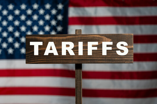 Tariffs sign on wooden plate with USA flag background. Closeup of wooden signpost with text tariffs on blurred american flag background usa economy global trade tax war politics concept