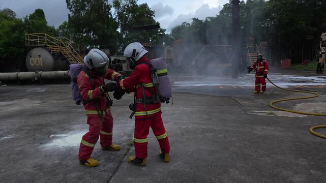 Firefighter fire training rescue industrial smoke hose safety drill on concrete yard, protective suit breathing apparatus water spray, emergency response foam attack exercise with equipment