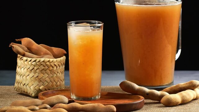 Fresh iced tamarind drink in a glass with pitcher and whole tamarind pods
