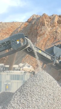Stone crushing machine at open pit mining and processing plant for crushed stone. Piles of gravel stone and conveyor belts. Excavator loading rocks. Concepts of industry and building materials