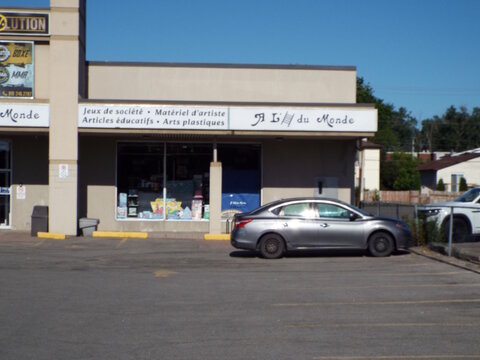Gatineau, Quebec, Canada &ndash; June 21, 2026: A grey sedan is parked in front of the "&Agrave; L'&Eacute;chelle du Monde" storefront in a sunny parking lot at 74 Bd Gr&eacute;ber.