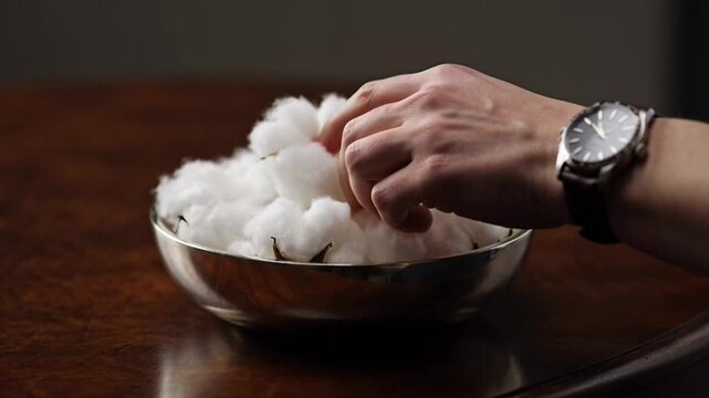 A close up shot of a hand reaching into a silver bowl filled with soft white cotton balls.
