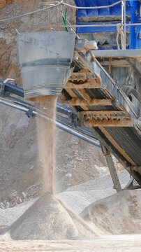 Stone crushing machine at open pit mining and processing plant for crushed stone. Piles of gravel stone and conveyor belts. Excavator loading rocks. Concepts of industry and building materials