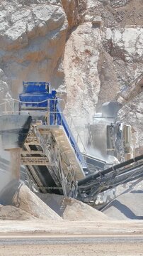 Stone crushing machine at open pit mining and processing plant for crushed stone. Piles of gravel stone and conveyor belts. Excavator loading rocks. Concepts of industry and building materials